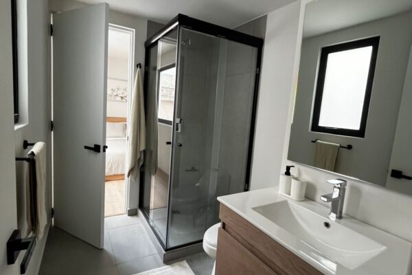 Spacious bathroom with a modern sink, large mirror, and glass shower enclosure, illuminated by natural light.