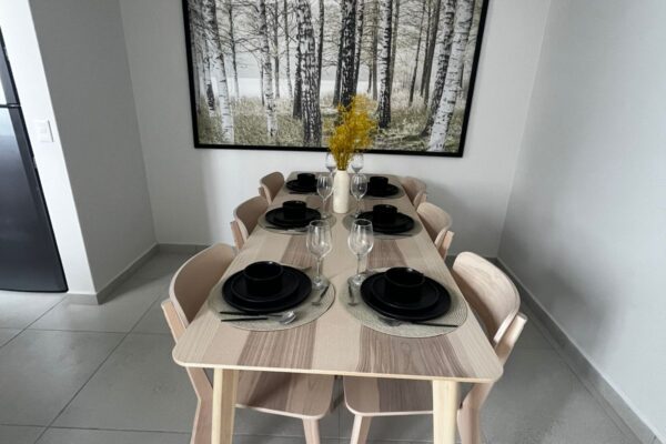 Modern dining area with a minimalist table, wooden chairs, and black dishware, complemented by a birch tree artwork.