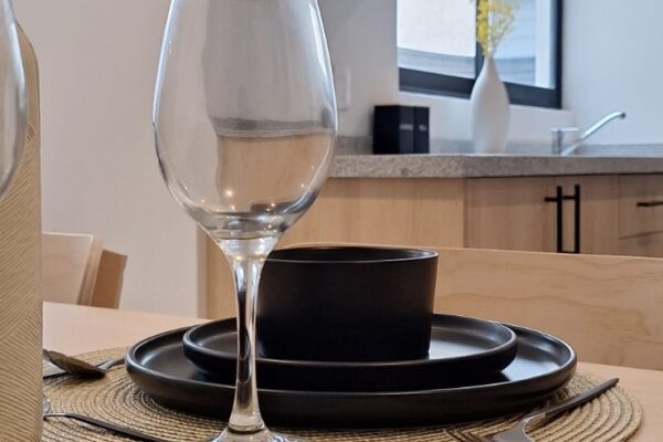 Close-up of a table setting featuring black dishware and wine glasses on woven placemats, emphasizing clean and modern design.