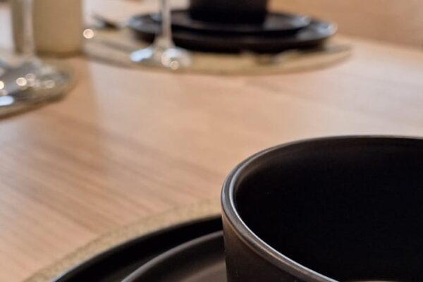 Detailed view of black dishware on a light wooden table, paired with sleek silverware for a minimalist aesthetic.