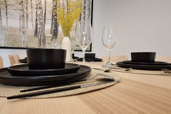 Elegant table setting with black dishware, wine glasses, and a decorative vase featuring yellow flowers, set against a birch tree artwork.