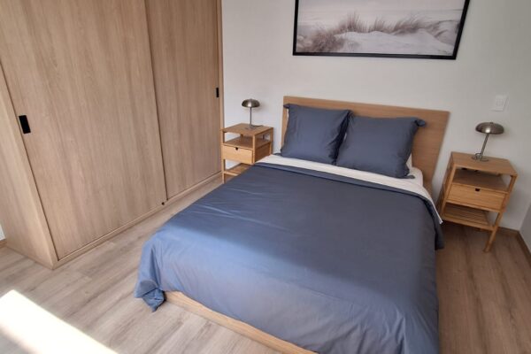 Minimalist bedroom with wooden furniture, a navy-blue bedspread, and a nature-inspired wall art.